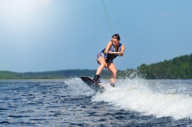 Slim brunette woman riding wakeboard on motorboat wave in lake clipart