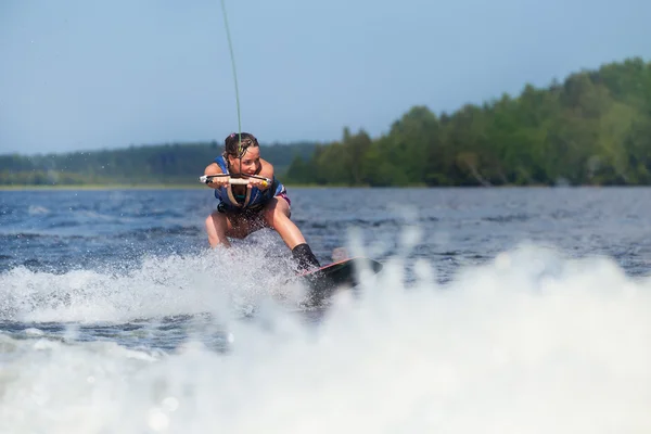 Slim brunette woman riding wakeboard on motorboat wave in lake — Stock Photo, Image