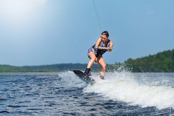 Schlanke brünette Frau reitet Wakeboard auf Motorbootwelle im See — Stockfoto