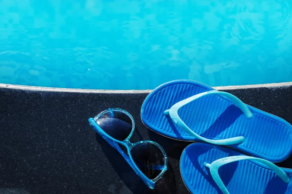 Blaue Hausschuhe und Sonnenbrille am Rand eines Swimmingpools — Stockfoto