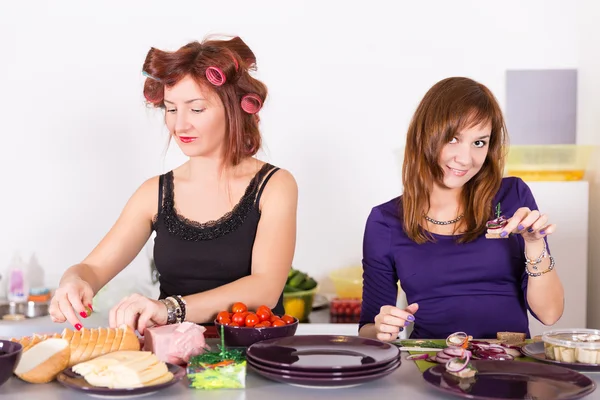 Zwei junge hübsche Hausfrauen kochen mit Lockenwicklern auf Haaren — Stockfoto