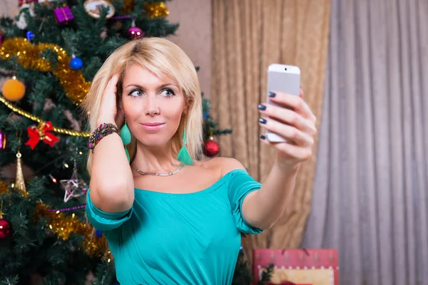 クリスマス ツリーの近くに携帯電話の selfie 写真を撮ってきれいな女性 — ストック写真