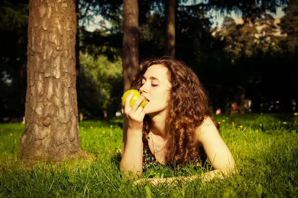 Beautiful young woman eating apple outdoors — Stock Photo, Image