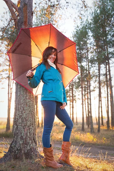 Jovem com guarda-chuva em luzes de pôr do sol na floresta — Fotografia de Stock