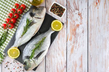 Beyaz ahşap arka planda taze balık dorado 'su. Yemek pişirmek için malzemeler de var.