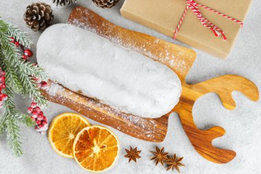 Klasik Noel Stollen, ahşap tahtada kurutulmuş portakallar, çam dalları ve beyaz desenli arka planda koniler ile pudra şekerli kremayla kaplıdır. Geleneksel bayram yemeği, tatlı meyveli ekmek.