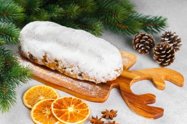 Klasik Noel Stollen, ahşap tahtada kurutulmuş portakallar, çam dalları ve beyaz desenli arka planda koniler ile pudra şekerli kremayla kaplıdır. Geleneksel bayram yemeği, tatlı meyveli ekmek.