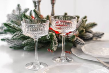 Arka planda iki zarif kristal bardak ve buzlu her zaman yeşil olan düzenleme, estetik bir Noel ve yeni yıl sofra kurumu, şenlik ruhu ve kış tatili kutlamalarının sıcaklığı yaratıyor..