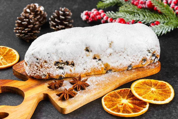 Klasik Noel Stollen, ahşap tahtada kurutulmuş portakallar, siyah desenli yüzey üzerinde çam dalları ve koniler ile pudra şekerli kremayla kaplıdır. Geleneksel bayram yemeği, tatlı meyveli ekmek.