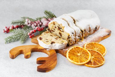 Geleneksel Noel süslemesi, ahşap tahtada dilimlenmiş tatlı meyve somunu, beyaz desenli arka planda pudra şekeri ile tozlanmış. Baharatlar, kurutulmuş meyveler ve şenlikli dekorasyonlar kış tatili havası yaratır.