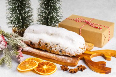 Klasik Noel Stollen, ahşap tahtada kurutulmuş portakallar, çam dalları ve beyaz desenli arka planda koniler ile pudra şekerli kremayla kaplıdır. Geleneksel bayram yemeği, tatlı meyveli ekmek.