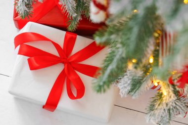 Güzel bir hediye, zarif beyaz bir kağıda sarılmış yeşil karlı Noel ağacının altında kırmızı bir fiyonk ve sıcak ışıklar. Sıcak kış tatili atmosferi mevsimlik kutlamalar için mükemmel.