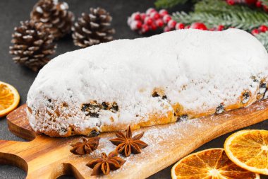 Klasik Noel Stollen, ahşap tahtada kurutulmuş portakallar, siyah desenli yüzey üzerinde çam dalları ve koniler ile pudra şekerli kremayla kaplıdır. Geleneksel bayram yemeği, tatlı meyveli ekmek.