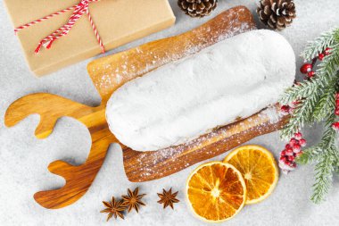 Klasik Noel Stollen, ahşap tahtada kurutulmuş portakallar, çam dalları ve beyaz desenli arka planda koniler ile pudra şekerli kremayla kaplıdır. Geleneksel bayram yemeği, tatlı meyveli ekmek.