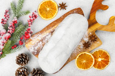 Klasik Noel Stollen, ahşap tahtada kurutulmuş portakallar, çam dalları ve beyaz desenli arka planda koniler ile pudra şekerli kremayla kaplıdır. Geleneksel bayram yemeği, tatlı meyveli ekmek.