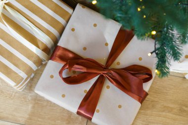 Güzel bir hediye, zarif beyaz bir kağıda sarılmış yeşil karlı Noel ağacının altında sıcak ışıklarla. Sıcak kış tatili atmosferi mevsimlik kutlamalar ve dekor temaları için mükemmel