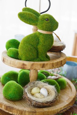 Yeşil yosun Paskalya Tavşanı ve dekoratif Paskalya yumurtaları yuvanın arka planında iki katlı ahşap tabakta. Bahar tatilleri için ev dekorasyonu, şenlik masası.