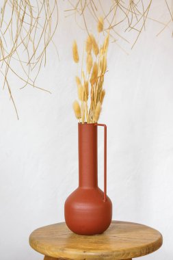 Basit el yapımı çanak çömlek ve beyaz alçılı kurumuş dallar, sıva duvar arkaplanı. Doğal ışık sıcak dokuları vurguluyor. Sakin ev havası için en az iç kompozisyonu oluşturuyor..