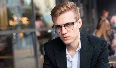 Çekici, genç, ciddi, gözlüklü bir adam kameraya bakıyor.