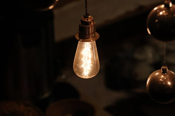 Old dusty incandescent lamp bulb on the wire shines in the dark and mirror balls around — Stock Photo, Image