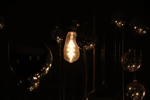 Stará zaprášená žárovka na drátě svítí ve tmě a zrcadlových koulích kolem — Stock fotografie