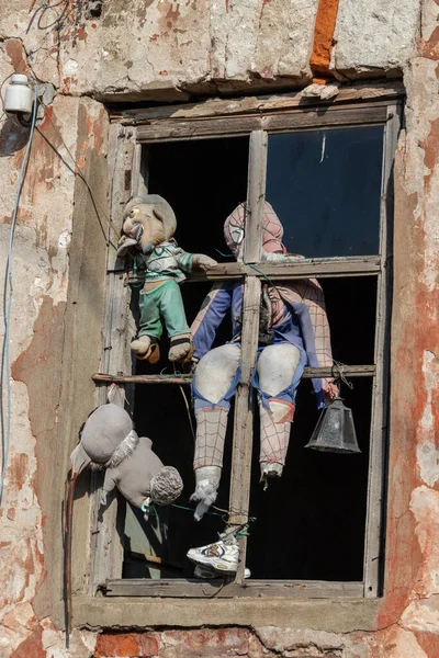 Terk edilmiş eski bir evin turuncu duvarında, ahşap bir pencerede duran eski ve garip bir oyuncak bebek. — Stok fotoğraf