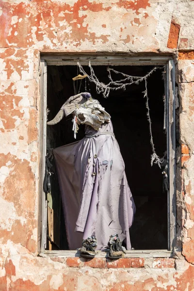 Eine seltsame alte zerrissene Puppe in einem Holzfenster in der orangefarbenen Wand eines alten, verlassenen Hauses — Stockfoto