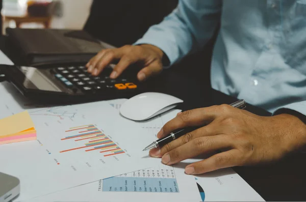 Business men hold pen and calculator to see graphs and report sales and business growth.Business document finance and statistics of profit in management.