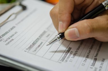 Masanın üzerinde kalem yazma başvuru belgeleri olan el..