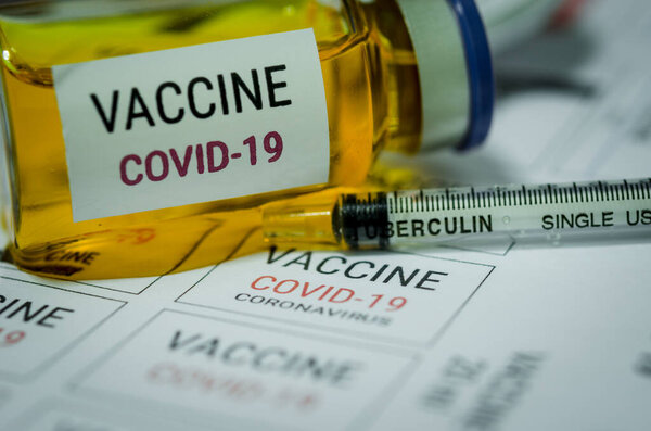 Medication labels and bottles of COVID-19 vaccine and syringe.