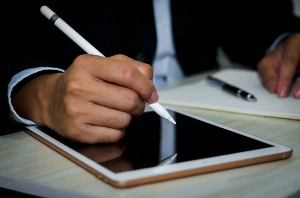 Business man holding a pen to take notes on the tablet on a desk.