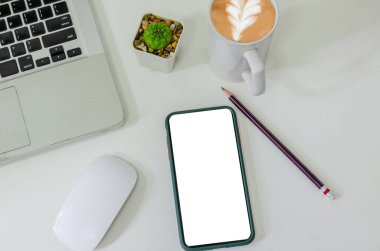Top view mock up smart phone white blank screen and pencil coffee cup mouse computer laptop flat lay on desk.