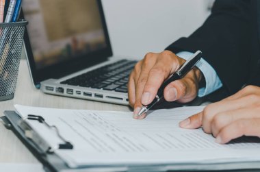İş adamı bilgisayarını ve kalem kağıtlarını kullanarak bir masayı belgeliyor. İş finansmanı, vergi ve yatırım kavramları.