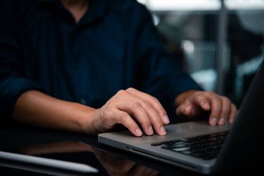 Karanlık bir çalışma alanında dizüstü bilgisayarda yazı yazan ellerin yakın çekimi. Çalışma odağı kavramı, uzak iş, veya programlama teknolojisi dijital dönüşüm, ve akıllı iş çözümleri.