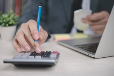 Hesap makinesi kullanan işadamı, kalem ve fatura ile mali rapor, muhasebe, vergi hesaplaması, gider yönetimi, bütçe planlaması ve kurumsal finans süreci üzerinde çalışıyor.