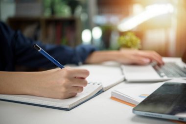 Masa başında okuyup çalışan, eğitim kitapları ve dizüstü bilgisayarı olan biri. Modern öğrenim ve üretkenlik, öğrenci hayatı kavramları, çevrimiçi eğitim ve kariyer gelişimi.