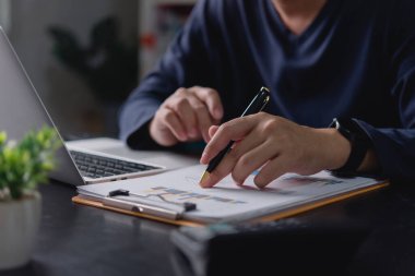 Finansal veri raporunu analiz eden bir işadamı elinde kalemle haritayı işaret ediyor. Dizüstü bilgisayarlı ofis masasında çalışan, iş performansını, yatırım büyümesini ve başarı için piyasa stratejisini inceleyen adam.