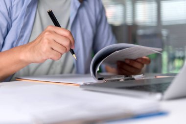 Ofis çalışanı belgeleri inceler, raporları analiz etmek ve görevleri düzenlemek için dizüstü bilgisayarın yanına notlar yazar. Yakın çekim eller doğruluk, odaklanma, planlama ve üretkenlik kavramını iletir.