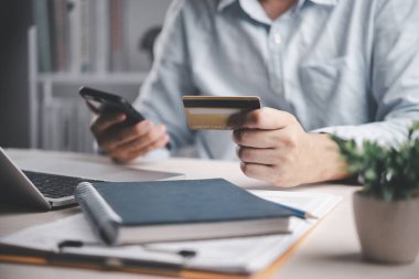 Adamın elinde kredi kartı, akıllı telefon, online alışveriş ödemesi. E-ticaret teknolojisi konsepti. Tüketici satın alma ürünü, mobil bankacılık, mali işlem, çalışma masası bilgisayarı, dijital yaşam tarzı.