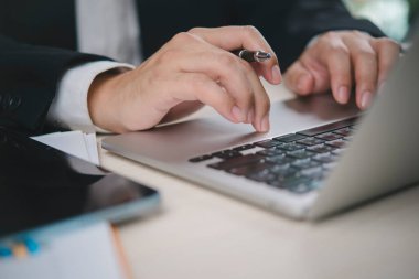 Yakın plan iş adamı çoklu görev, kalem tut, dizüstü bilgisayar kullan. Ofis masasında çalış. Profesyonel teknoloji, internette gezinme, klavye yazma. Veri analizi, proje yönetimi, uzaktan çalışma.