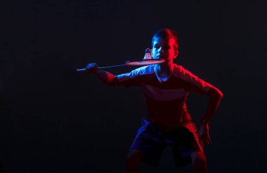 Badminton oynayan çocuk, siyah arka planda karışık ışıkta izole edilmiş. Mavi ve kırmızı filtre. Ürün gösterimi, afişi veya alay konusu için spor arkaplanı