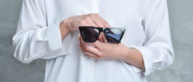 Güneş gözlüğü tutan bir kadının orta kısmı. Ürün görüntüleme, pankart veya alay için arkaplan