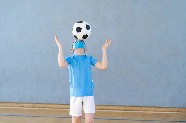 School kid with mask and soccer ball in a physical education lesson. Social distancing to fight COVID-19. Safe back to school during pandemic concept