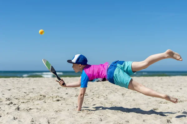 Genç çocuk sahilde tenis oynuyor. Yaz sporu.