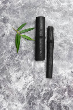 Bambu etkinleştirilmiş kömür çubukları ve gri arkaplanda izole edilmiş yeşil yaprak
