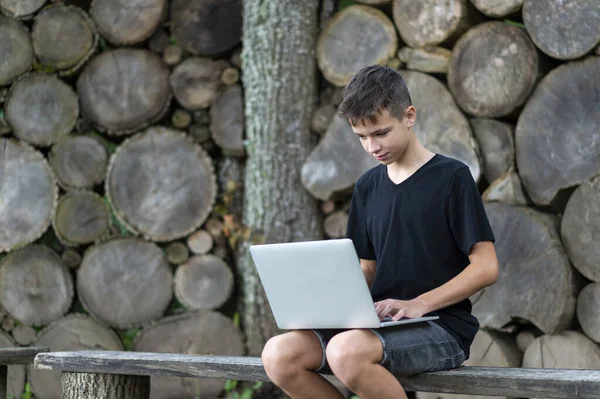 Boy sitting on wooden seat with laptop in forest. Kid have online web lesson or class on computer at nature, green class. Back to school. Outdoor learning concept