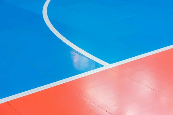 Mavi ve turuncu zemin voleybol, basketbol, badminton, futsal, hentbol sahası. Spor salonunun ahşap zemininde ahşap zemin çizgileri var.