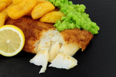 Battered cod fish fillet with chunky chips and mushy peas on a slate stone background clipart