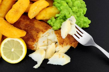 Dökülmüş balık filetosu, tombul patates kızartması ve kayrak taşı arka planında lapa bezelye.