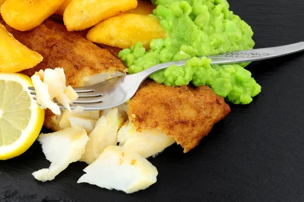 Battered cod fish fillet with chunky chips and mushy peas on a slate stone background